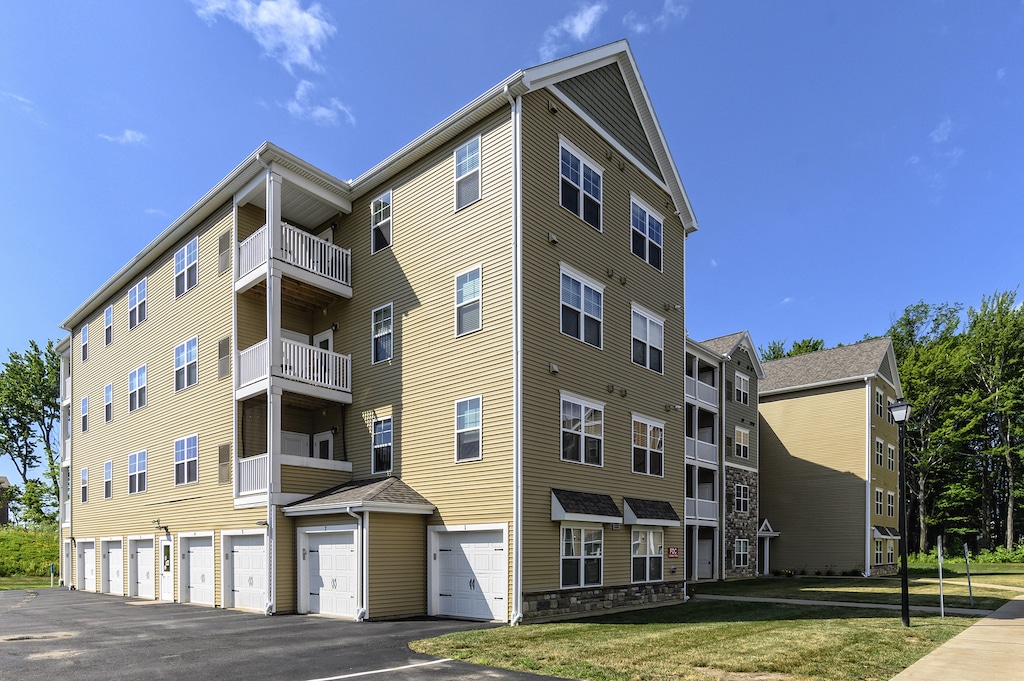 Four-story apartment building with beige siding, multiple balconies, and garage units on the ground level under a clear blue sky.