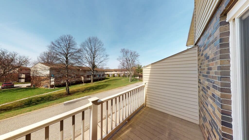 View from a balcony overlooking a quiet street with bare trees and residential buildings on a sunny day.