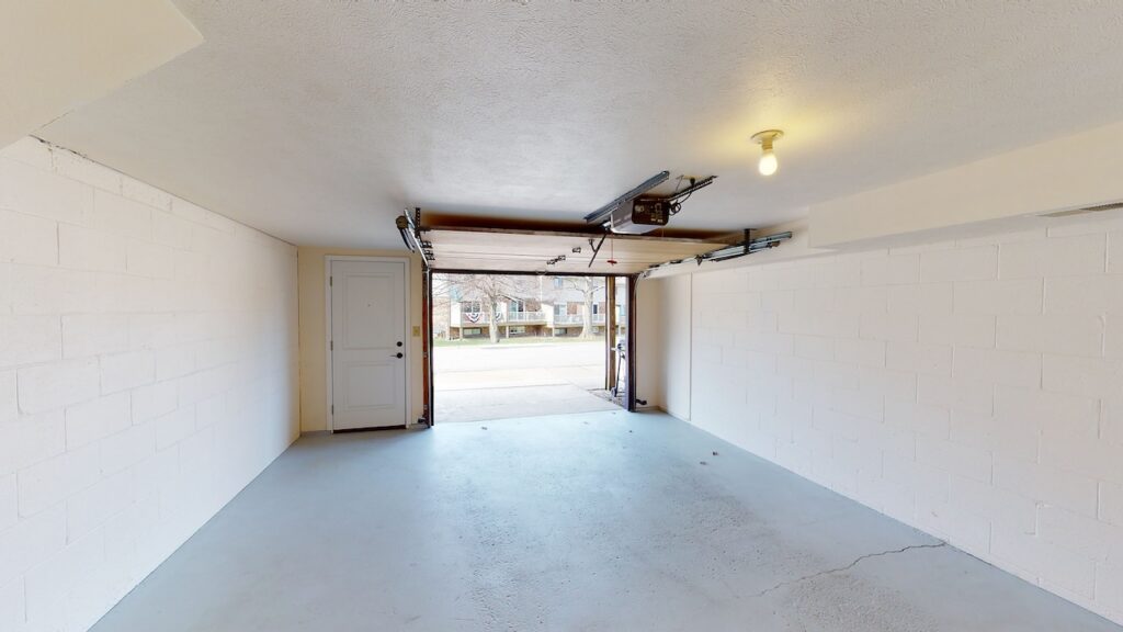 Empty garage with open door, white walls, and a single overhead lightbulb.