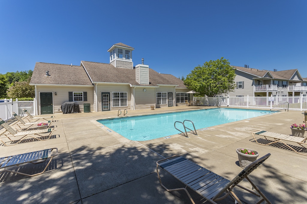 Outdoor swimming pool with lounge chairs and a clubhouse under a clear blue sky.