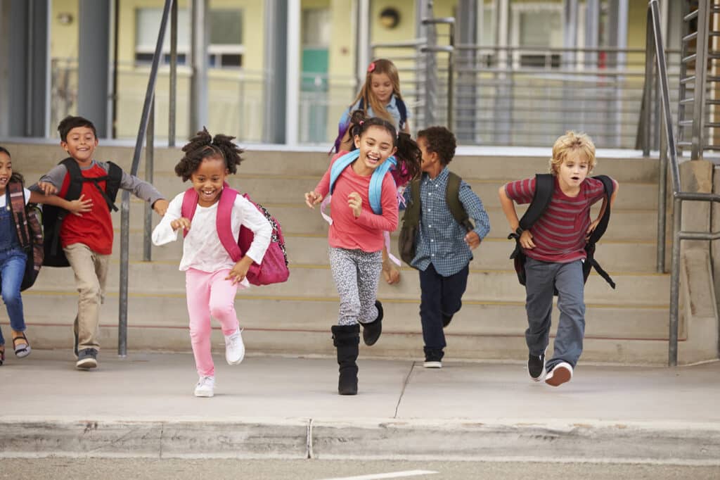 Children with backpacks happily running outside a building.