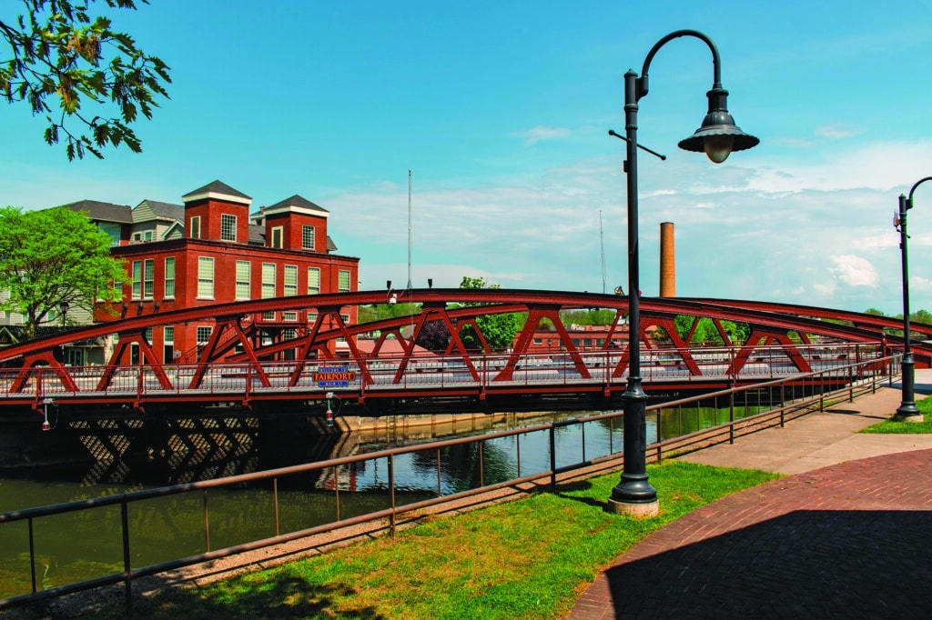 Red iron bridge over a canal with a brick building in the background 
Fairport Lift Bridge in New York