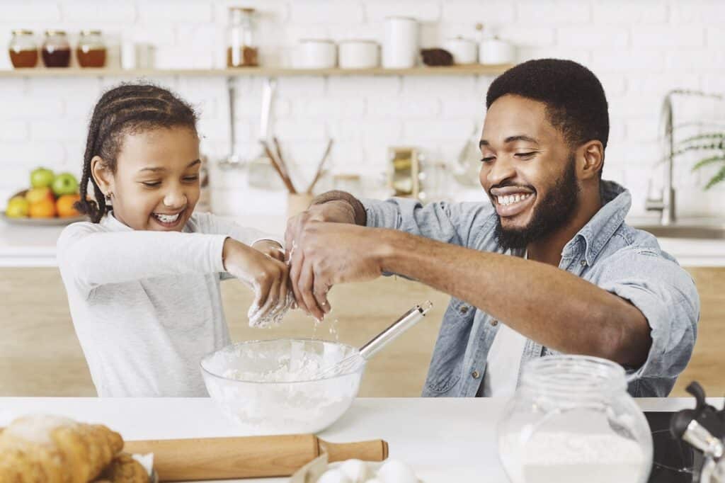 Father and daughter mixing dough in a kitchen, smiling and enjoying the activity together.