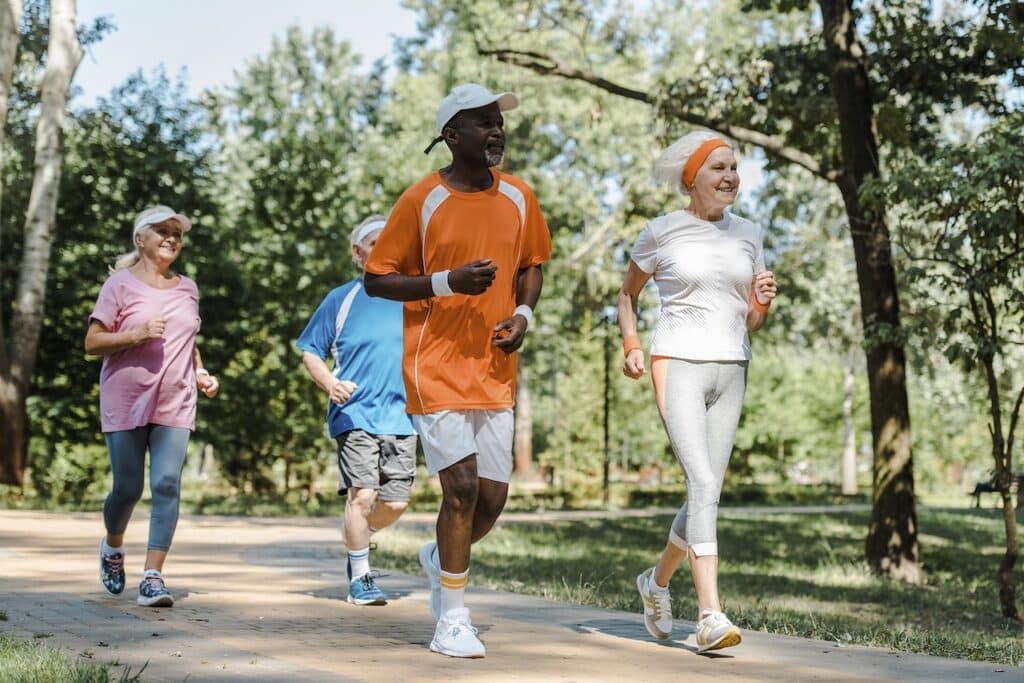 Four people jogging on a path through a park with trees in the background.