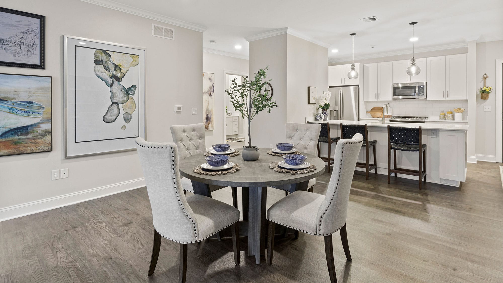 Modern kitchen and dining area with a round table, four upholstered chairs, artwork on walls, and a kitchen island with stools.