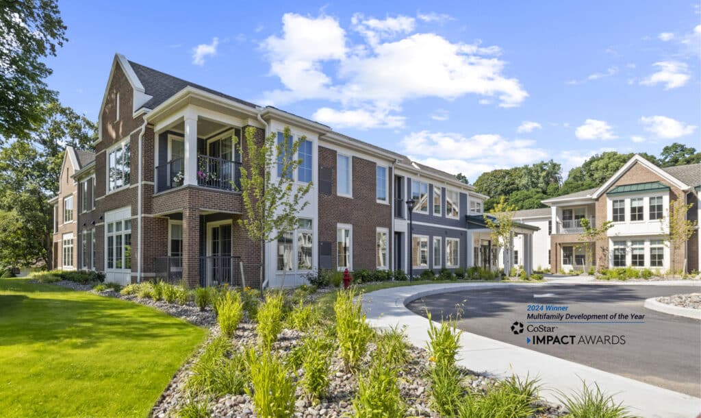 Luxury apartments in a modern multi-family development with a brick and siding facade, nestled in landscaped gardens. Award signage proudly displayed on the lawn showcases the prestige of these remarkable residences located in Pittsford, NY.