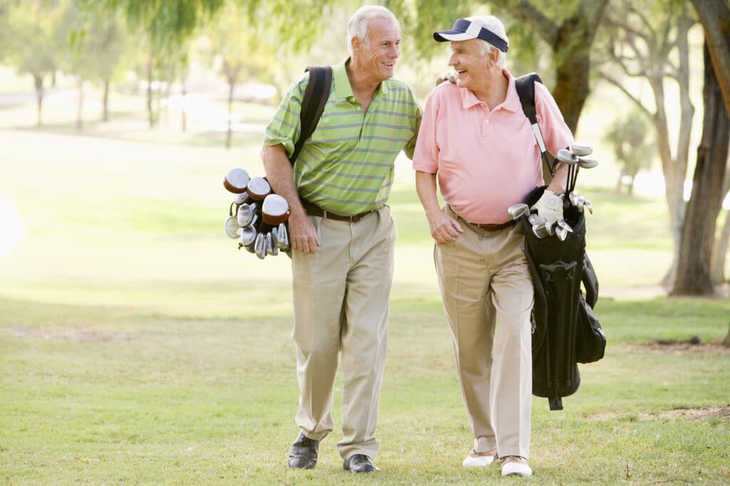 Two men walking on a golf course, each carrying a golf bag, smiling and engaged in conversation.