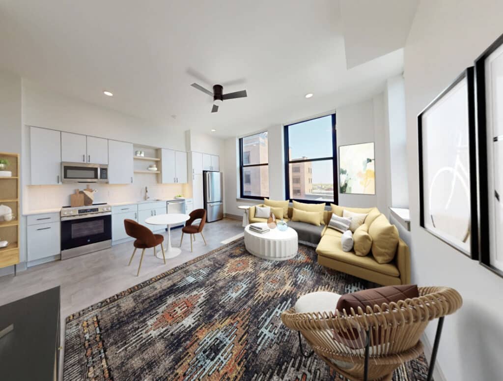 Open-concept living room and kitchen in a modern East End Rochester apartment at The Neisner, featuring large windows, contemporary finishes, and stylish staging.