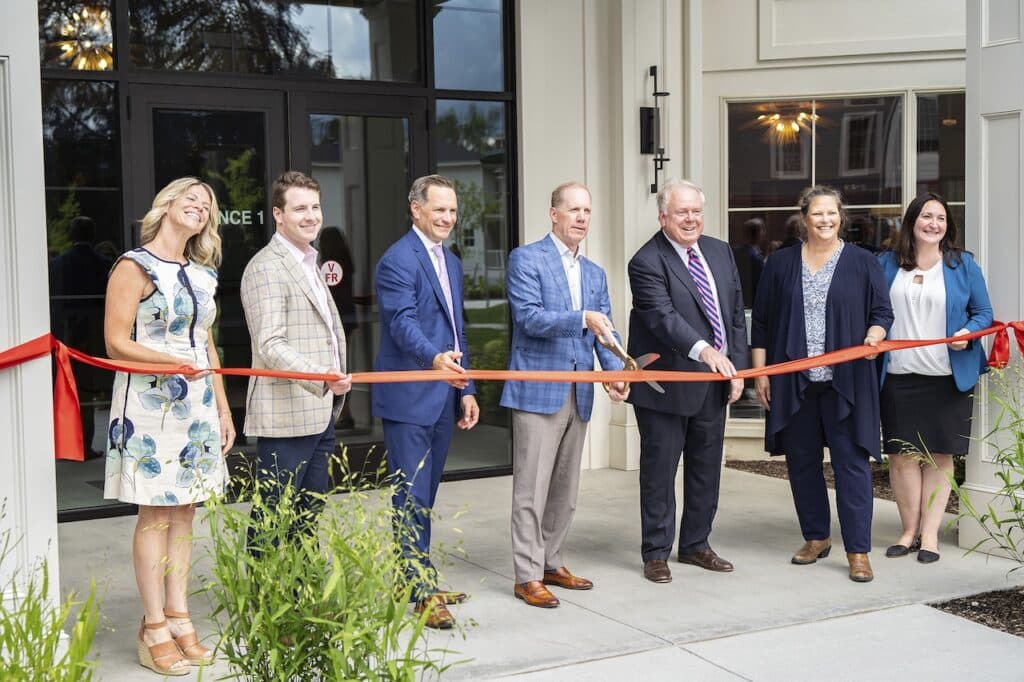 A group of people stand in front of a building as a ribbon is being cut during a ceremony.