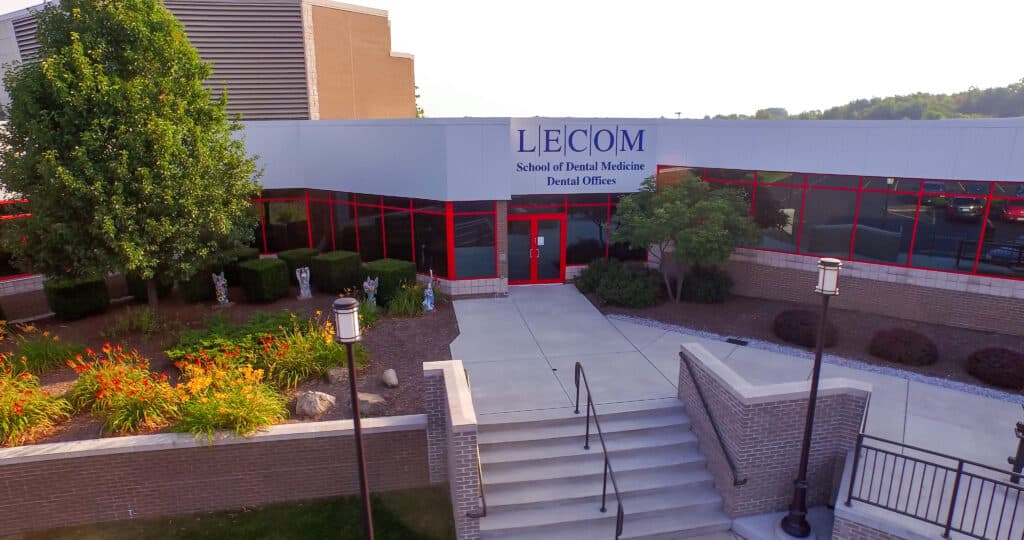 Entrance of LECOM School of Dental Medicine with red-framed glass doors and surrounding landscaping.