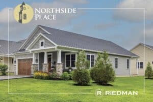 A modern single-story house with a gray roof and stone accents, surrounded by a neat lawn and shrubs. Logo in the corner reads "Northside Place," with "Riedman" at the bottom.