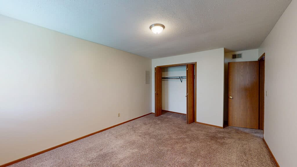Carpeted bedroom with an open closet featuring double doors, neutral walls, and a central light fixture. This inviting space offers ample room and flexibility for furniture arrangement at Royal Villa Apartments in Erie PA.