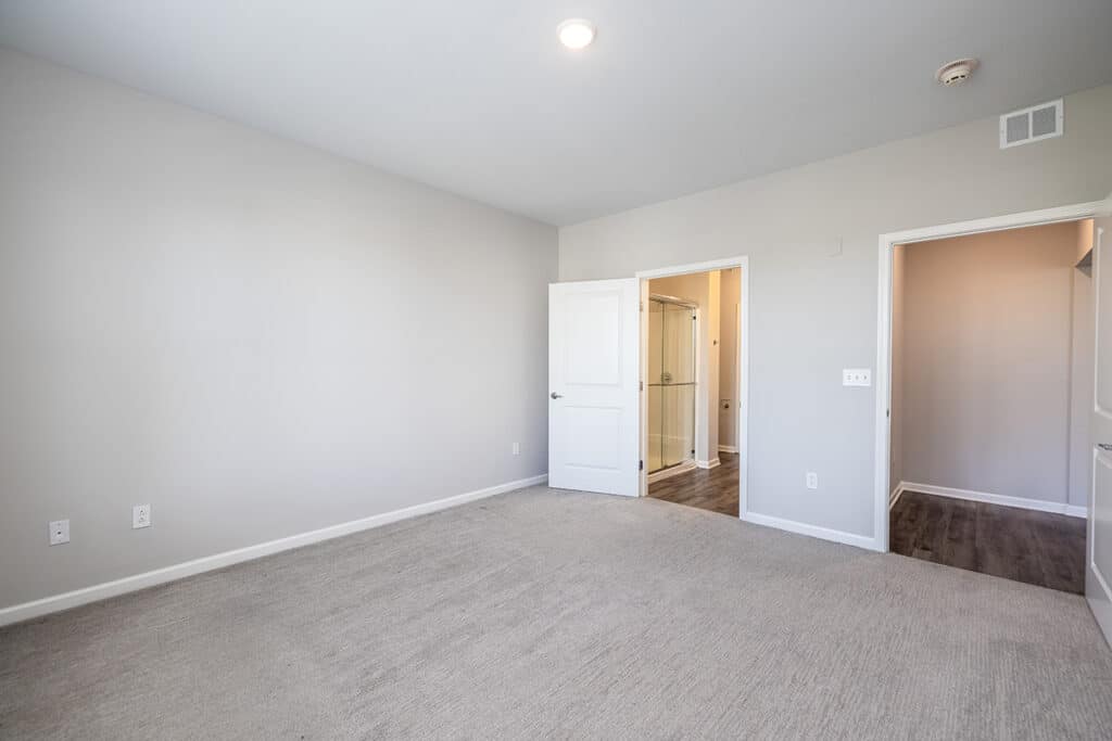A bright, master bedroom with light gray walls, carpeted floor, leading to a private master bathroom.