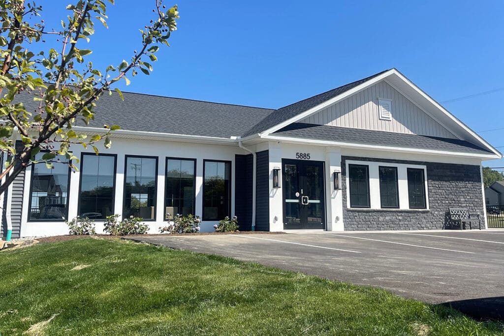 Front exterior of The Hammocks at Fairview resident clubhouse featuring modern architecture with stone accents, black framed windows, and landscaped entryway.