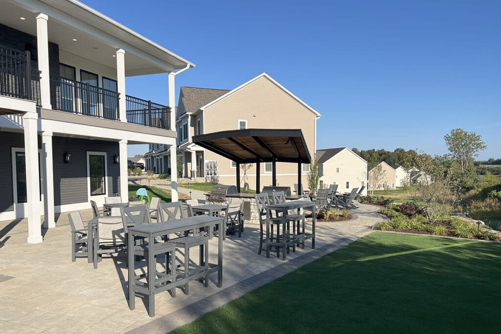 Spacious outdoor resident patio at The Hammocks at Fairview with bar-height tables, shaded seating, gas grills, and scenic views of the community surrounding the clubhouse.