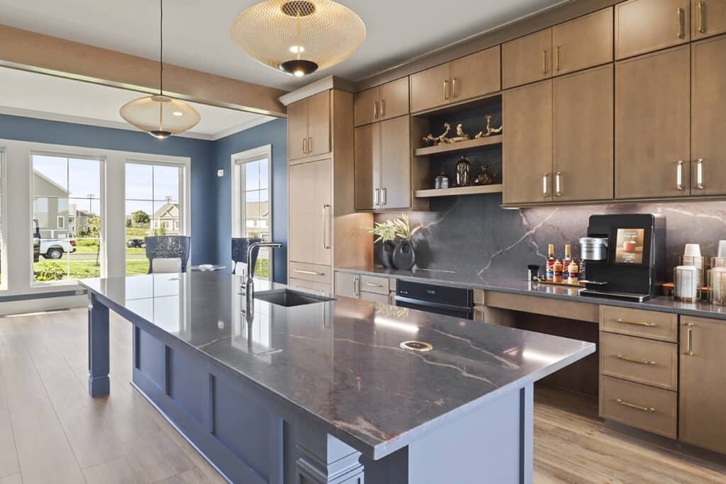 Stylish coffee café and kitchen area in The Hammocks at Fairview clubhouse, showcasing a large island with seating, wood cabinetry, modern pendant lighting, and a self-serve coffee station.