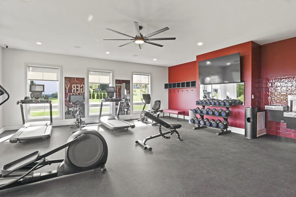 State-of-the-art fitness center inside the resident clubhouse at The Hammocks at Fairview, featuring treadmills, stationary bikes, free weights, a workout bench, and bright natural light from large windows.