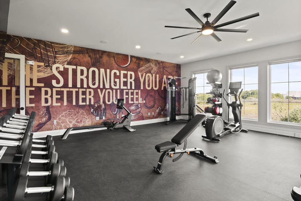 Spacious resident fitness center at The Hammocks at Fairview with strength training equipment, elliptical machines, a weight bench, and an accent wall reading “The Stronger You Are, The Better You Feel.”