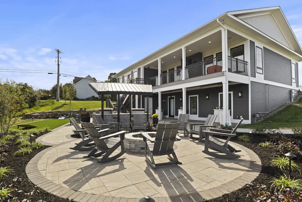 Inviting outdoor lounge area at The Hammocks at Fairview featuring Adirondack chairs around a stone firepit, covered seating area, and landscaped patio attached to the resident clubhouse.