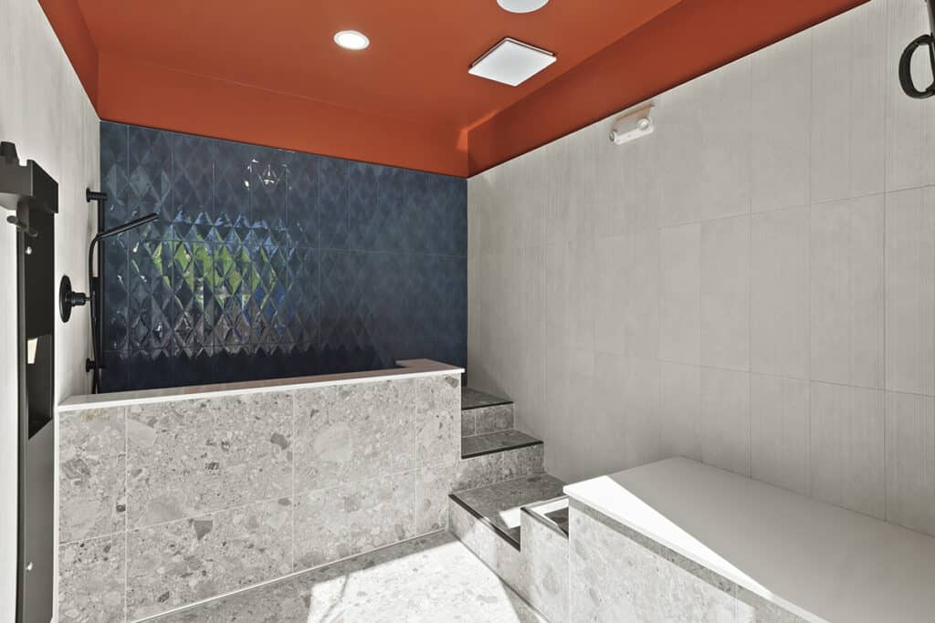 Modern pet spa at The Hammocks at Fairview located beside the mail and refuse center, featuring sleek tile walls, a raised wash station with steps for easy access, and a dark blue accent wall for a stylish, functional design.