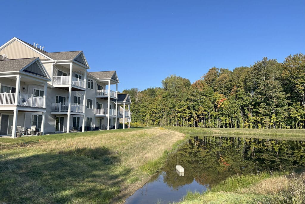 Apartment buildings at The Hammocks at Fairview overlooking a peaceful pond surrounded by trees, with private balconies offering relaxing natural views.