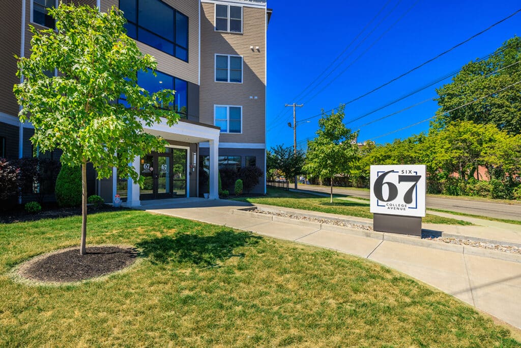 Six67 College Avenue exterior showing the front entrance, building façade, and community sign along College Avenue in Elmira, NY.