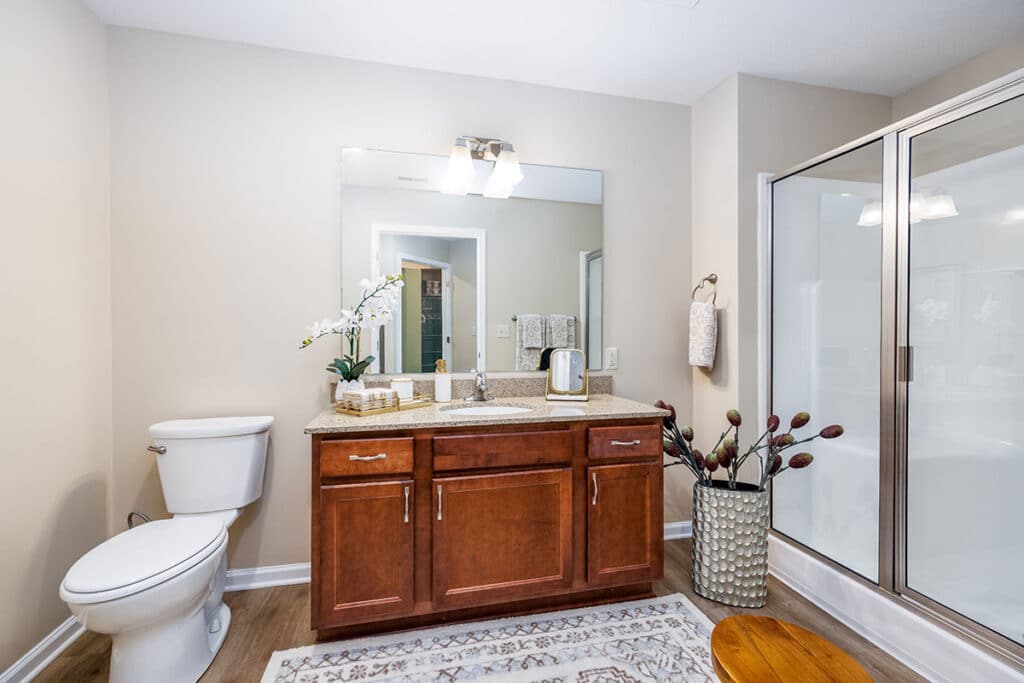 Full bathroom with oversized vanity, wood cabinetry, large mirror, toilet, and tub-shower combination at The Hammocks at Millcreek