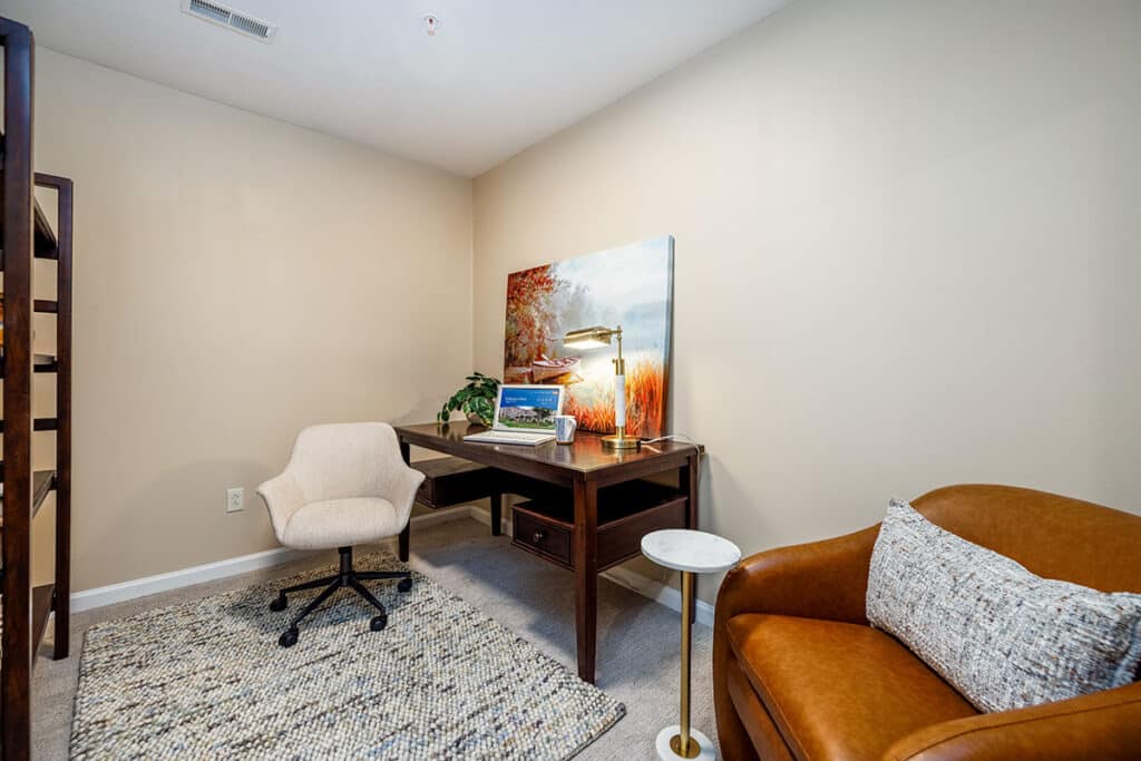 Flex space set up as a home office with desk, upholstered chair, accent seating, and neutral finishes at The Hammocks at Millcreek