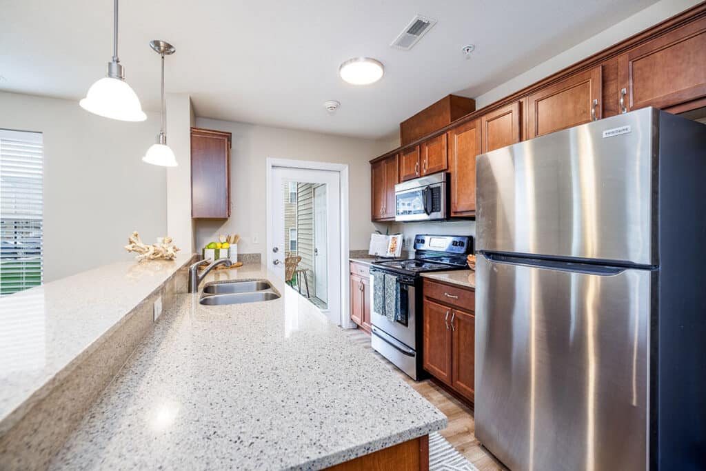 Kitchen detail with stainless steel microwave and refrigerator, electric range, wood cabinets, and quartz countertops and a door that leads to outside patio.