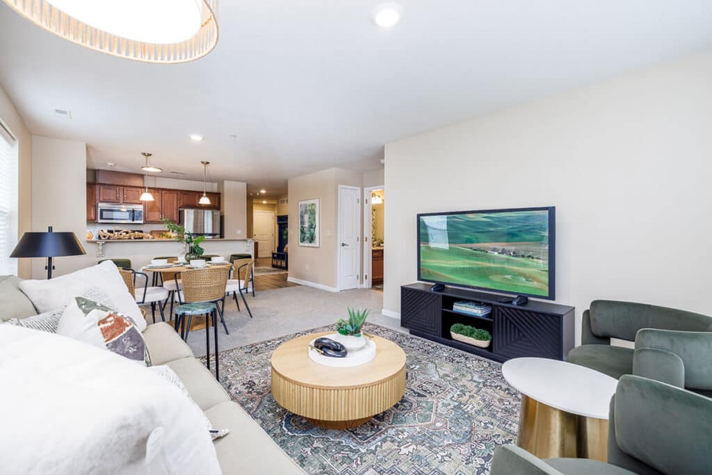 Spacious living room with sofa, accent chairs, large area rug, television, and open view into the kitchen and dining area