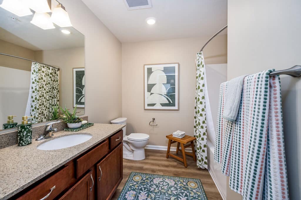Full bathroom with oversized vanity, wood cabinetry, large mirror, shower curtain, and luxury vinyl plank flooring