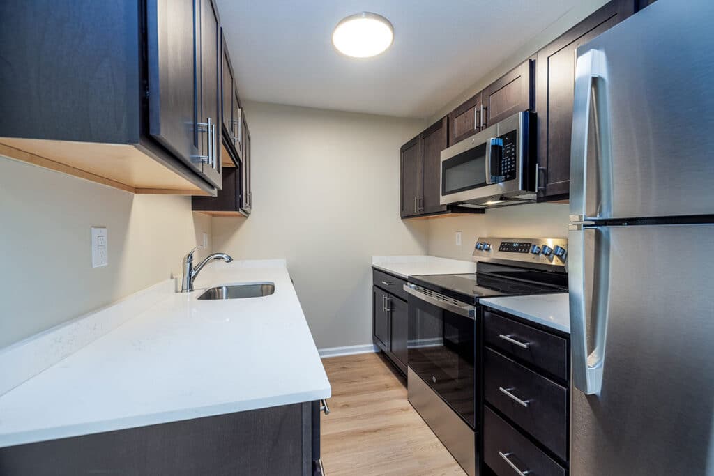 Updated kitchen at Royal Villa Apartments with stainless steel appliances, dark cabinetry, white countertops, and modern finishes.