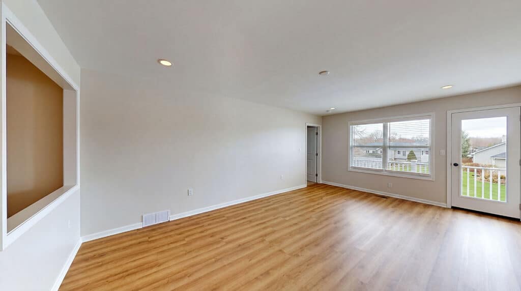 Empty room with light-colored walls, wood flooring, recessed ceiling lights, large window, and a glass door leading to a balcony with an outdoor view.