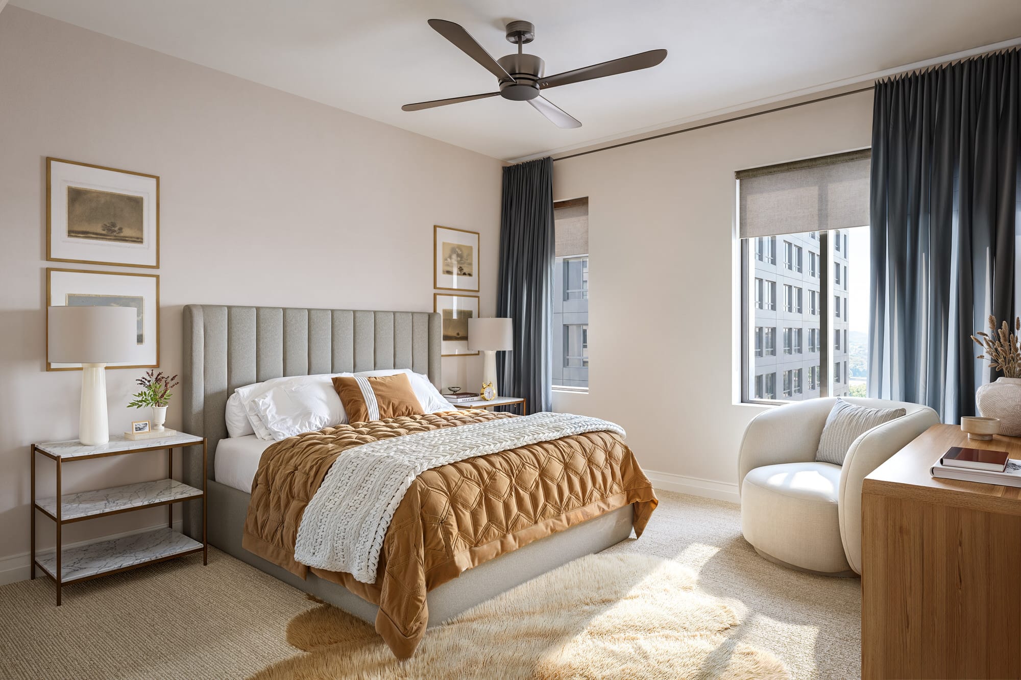 Modern bedroom with a neatly made bed, tan and white bedding, bedside tables with lamps, wall art, a ceiling fan, large windows, and neutral-colored decor.
