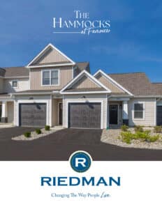 Two attached beige townhouses with double garages and landscaped yards under a clear blue sky, featuring signage for The Hammocks at Fairview and Riedman.